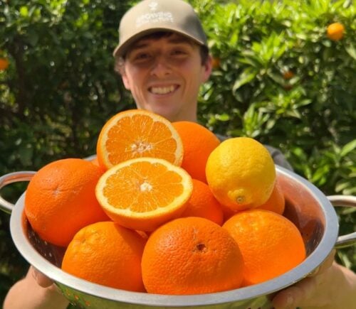 Vegan homesteader Luke Kelsall holding up a tub of oranges that he grew himself