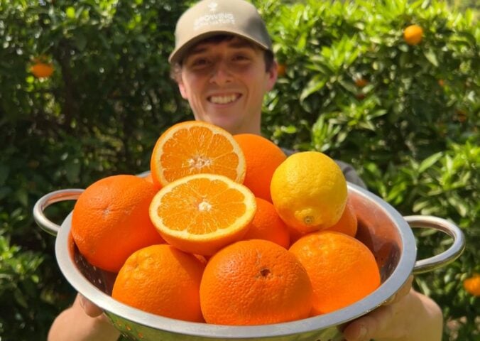 Vegan homesteader Luke Kelsall holding up a tub of oranges that he grew himself