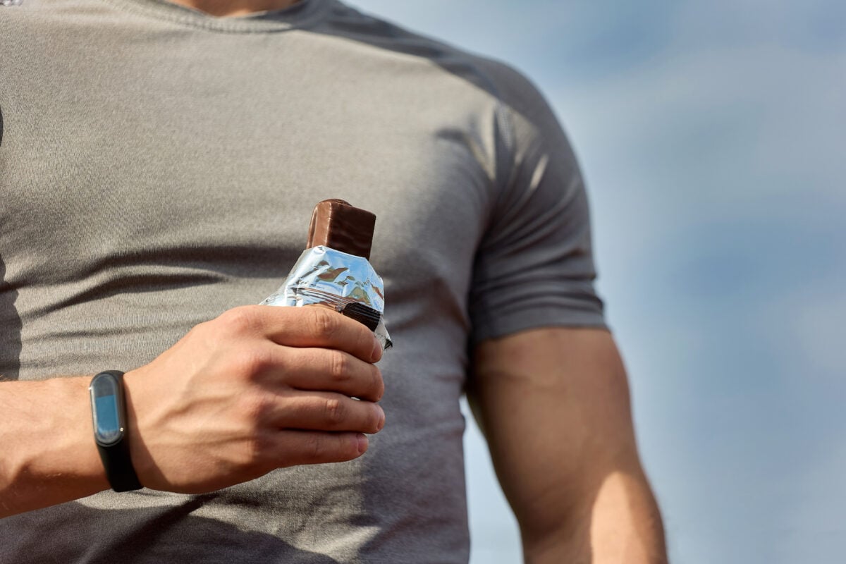 A muscular man eating a vegan protein bar