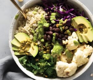 a warming cauliflower and quinoa bowl with avocado, black beans, basil pesto, and cauliflower