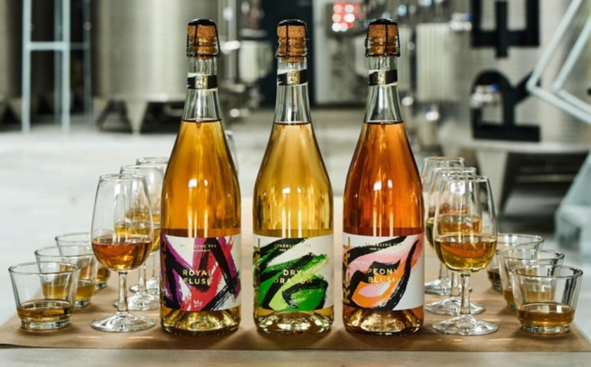 Photo shows three bottles of Real Drinks Co fizzy tea alongside wine glasses of the same