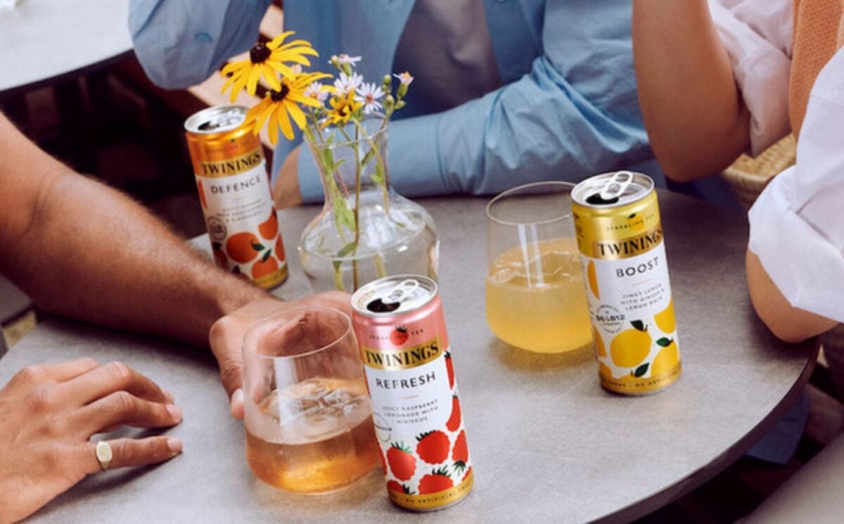 Photo shows a group of people sat at a table drinking tins of Twinings sparkling tea