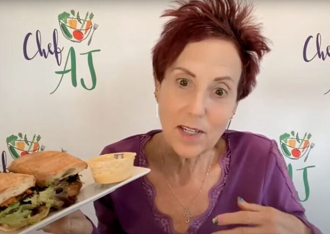 Chef AJ holding up a vegan sandwich, which she describes