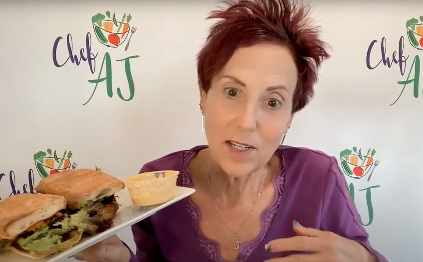 Chef AJ holding up a vegan sandwich, which she describes