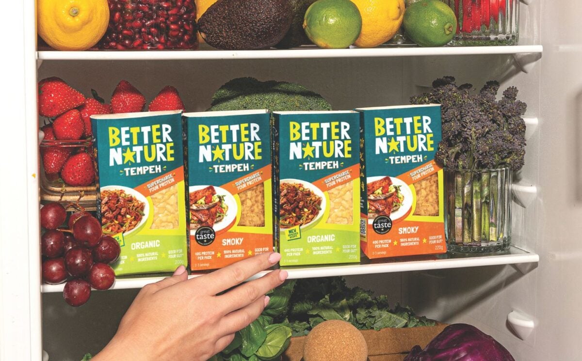 Photo shows someone's hand as they reach into a pantry, stocked with the full Better Nature tempeh range