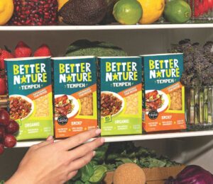 Photo shows someone's hand as they reach into a pantry, stocked with the full Better Nature tempeh range