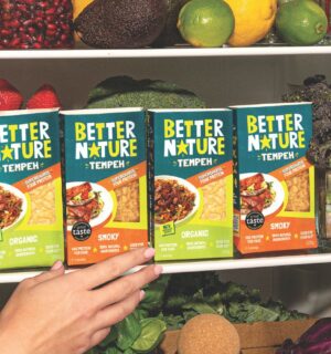 Photo shows someone's hand as they reach into a pantry, stocked with the full Better Nature tempeh range