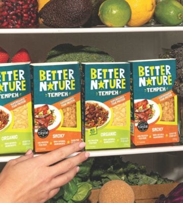 Photo shows someone's hand as they reach into a pantry, stocked with the full Better Nature tempeh range