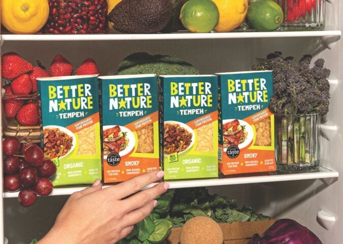 Photo shows someone's hand as they reach into a pantry, stocked with the full Better Nature tempeh range