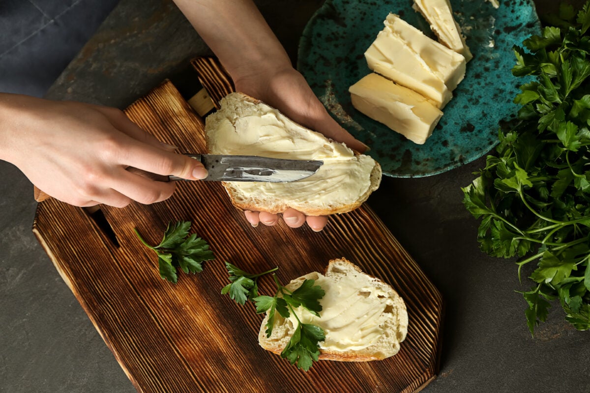 Photo shows someones hands as they spread butter on a slice of bread