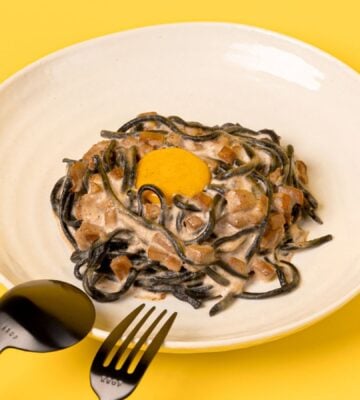 a bowl of charcoal spaghetti carbonara with vegan egg yolk and mushroom pancetta