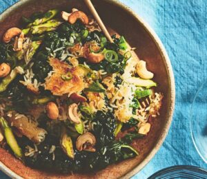 a bowl of crispy rice salad with crunchy vegetables and a side of cashew nuts