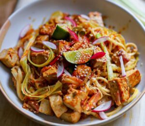 a bowl of crispy tofu stir fry with leek and chili topped with lime