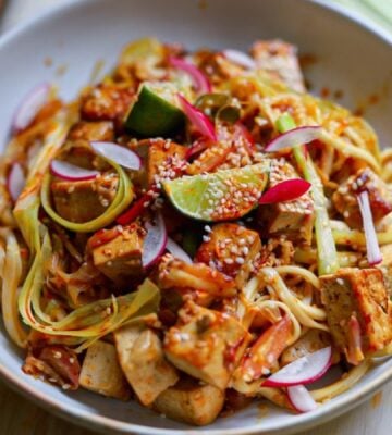 a bowl of crispy tofu stir fry with leek and chili topped with lime