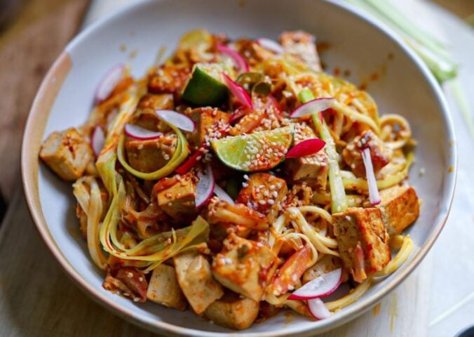 a bowl of crispy tofu stir fry with leek and chili topped with lime