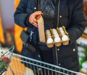 Photo shows a woman opening a large box of eggs while in a supermarket with a shopping trolley