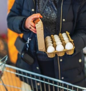 Photo shows a woman opening a large box of eggs while in a supermarket with a shopping trolley