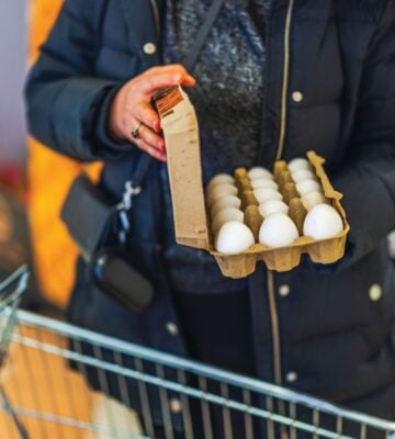 Photo shows a woman opening a large box of eggs while in a supermarket with a shopping trolley