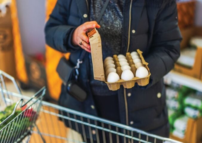 Photo shows a woman opening a large box of eggs while in a supermarket with a shopping trolley