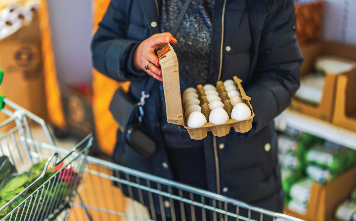 Photo shows a woman opening a large box of eggs while in a supermarket with a shopping trolley