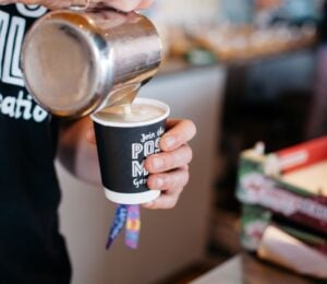Photo shows a barista pouring Oatly into a cup of coffee from a jug