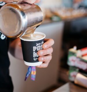 Photo shows a barista pouring Oatly into a cup of coffee from a jug