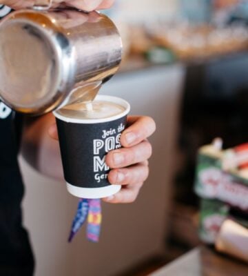 Photo shows a barista pouring Oatly into a cup of coffee from a jug