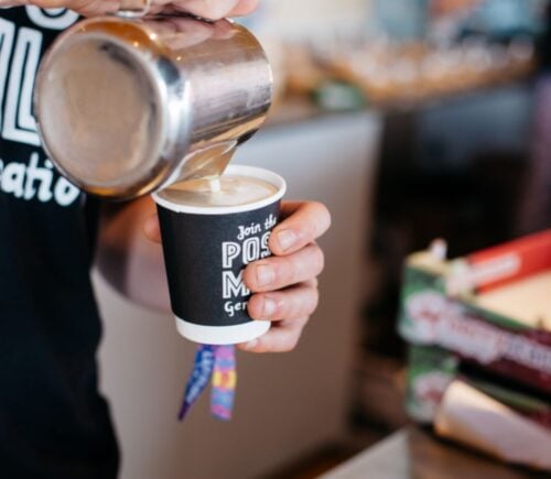 Photo shows a barista pouring Oatly into a cup of coffee from a jug