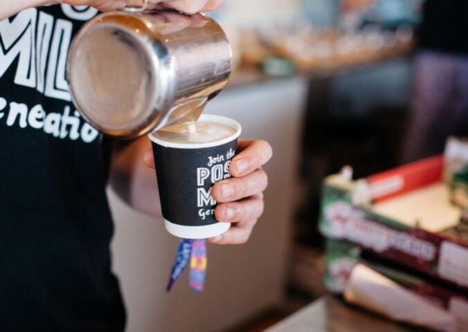 Photo shows a barista pouring Oatly into a cup of coffee from a jug