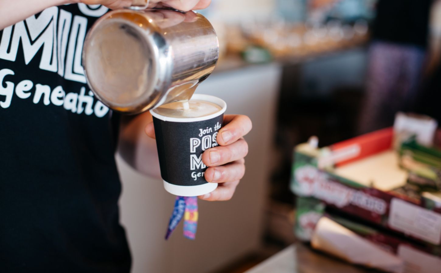 Photo shows a barista pouring Oatly into a cup of coffee from a jug