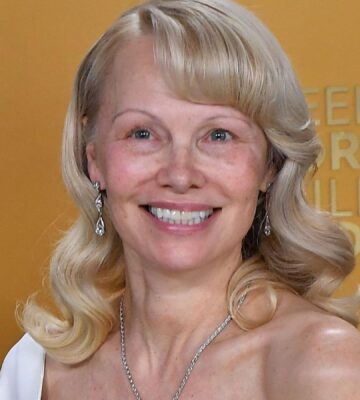 Photo shows Pamela Anderson at a media event standing against a gold background