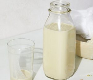 a picture of a bottle of perfect pistachio milk with s glass, cheesecloth, and whole pistachio nuts