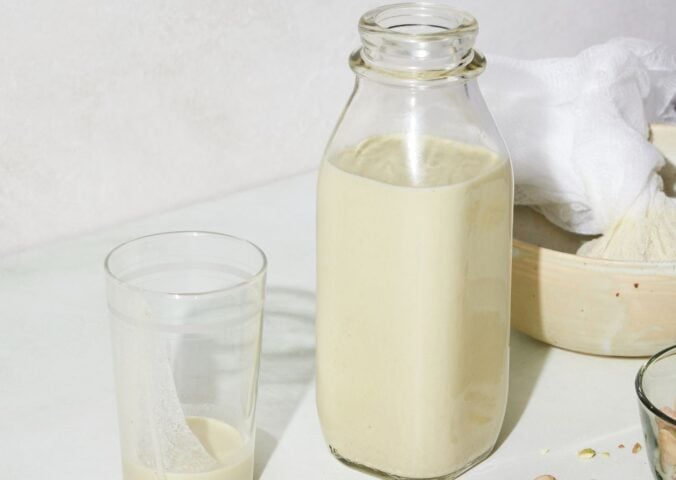 a picture of a bottle of perfect pistachio milk with s glass, cheesecloth, and whole pistachio nuts