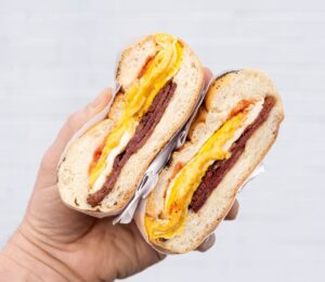 Photo shows someone's hand as they hold a bacon, egg, and cheese in a bagel - a popular NYC breakfast sandwich