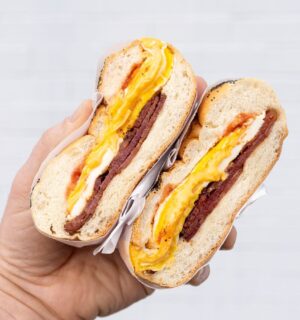Photo shows someone's hand as they hold a bacon, egg, and cheese in a bagel - a popular NYC breakfast sandwich
