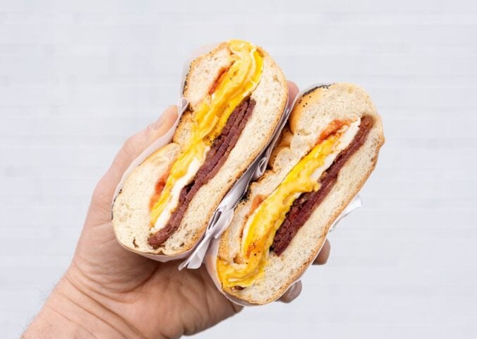 Photo shows someone's hand as they hold a bacon, egg, and cheese in a bagel - a popular NYC breakfast sandwich