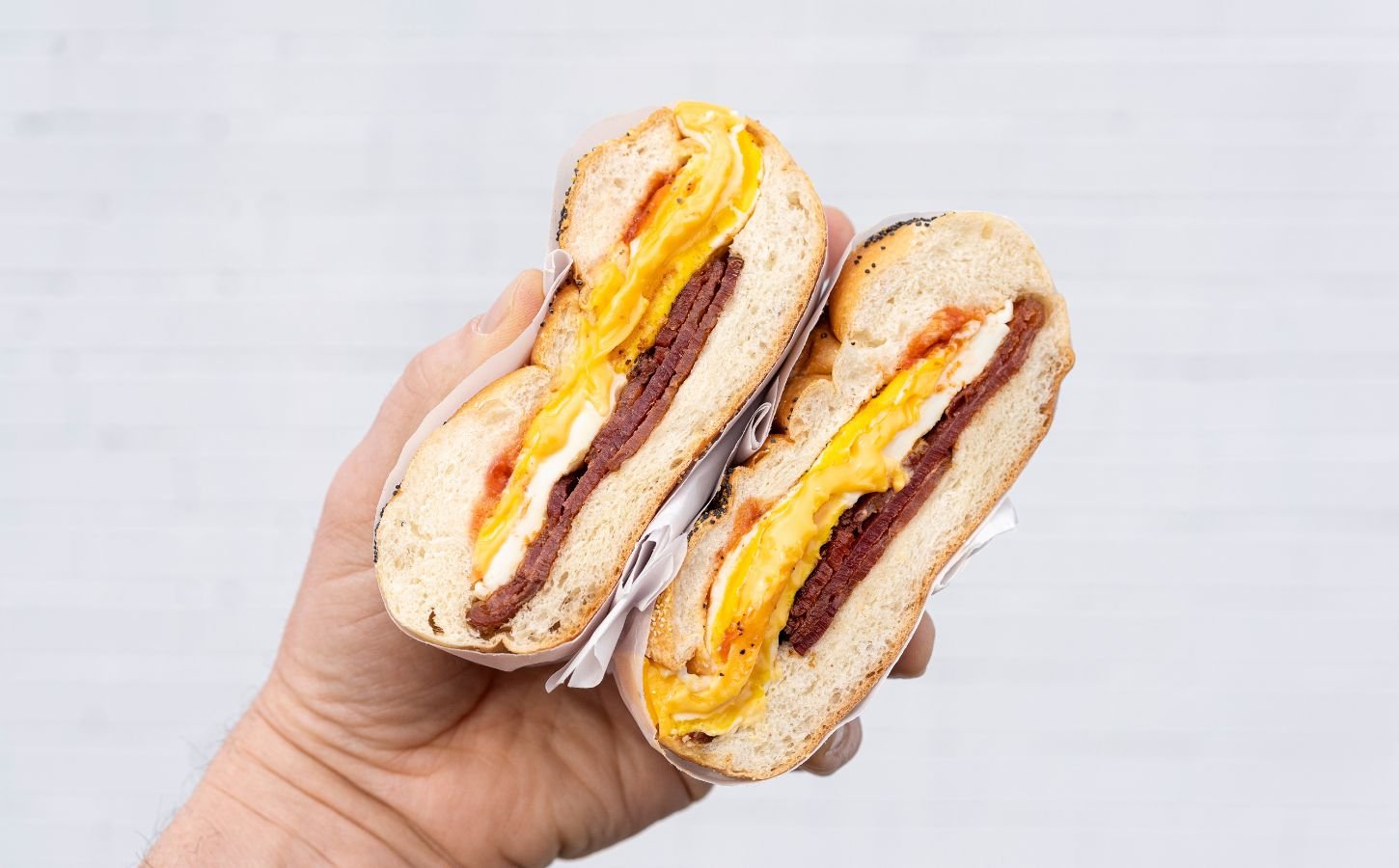 Photo shows someone's hand as they hold a bacon, egg, and cheese in a bagel - a popular NYC breakfast sandwich