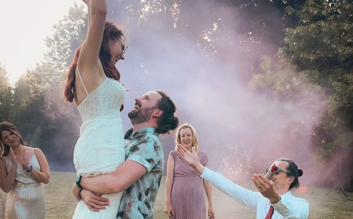 Photo shows Jason lifting Holly up at their vegan wedding while other members of the wedding party celebrate