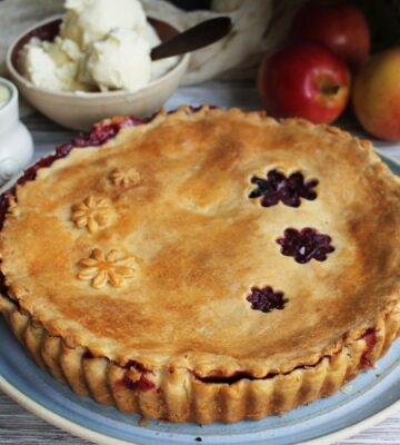 A vegan apple and blackberry pie next to some dairy-free cream and ice cream
