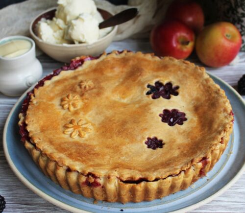 A vegan apple and blackberry pie next to some dairy-free cream and ice cream