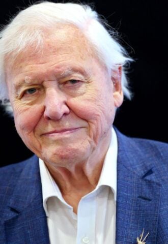 Photo shows Sir David Attenborough standing against a black background