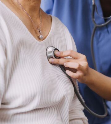 Photo shows a Dr or other healthcare professional using a stethoscope on a patient