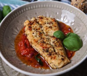 Photo shows two fillets of the latest Revo Foods product, vegan black cod, in a dish with a tomato-based sauce and green garnish