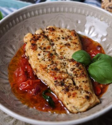 Photo shows two fillets of the latest Revo Foods product, vegan black cod, in a dish with a tomato-based sauce and green garnish