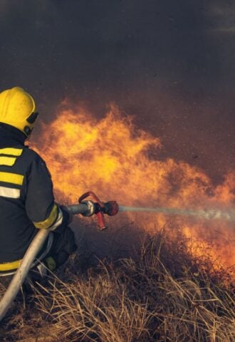 Photo shows a firefighting using a hose to fight a wildfire