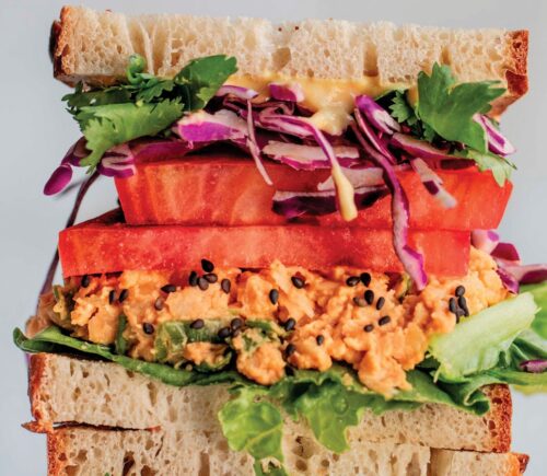 a picture of stacked peanut miso chickpea salad sandwiches with sesame, tomato, chickpea spread, and greens as part of vegan spring lunch ideas