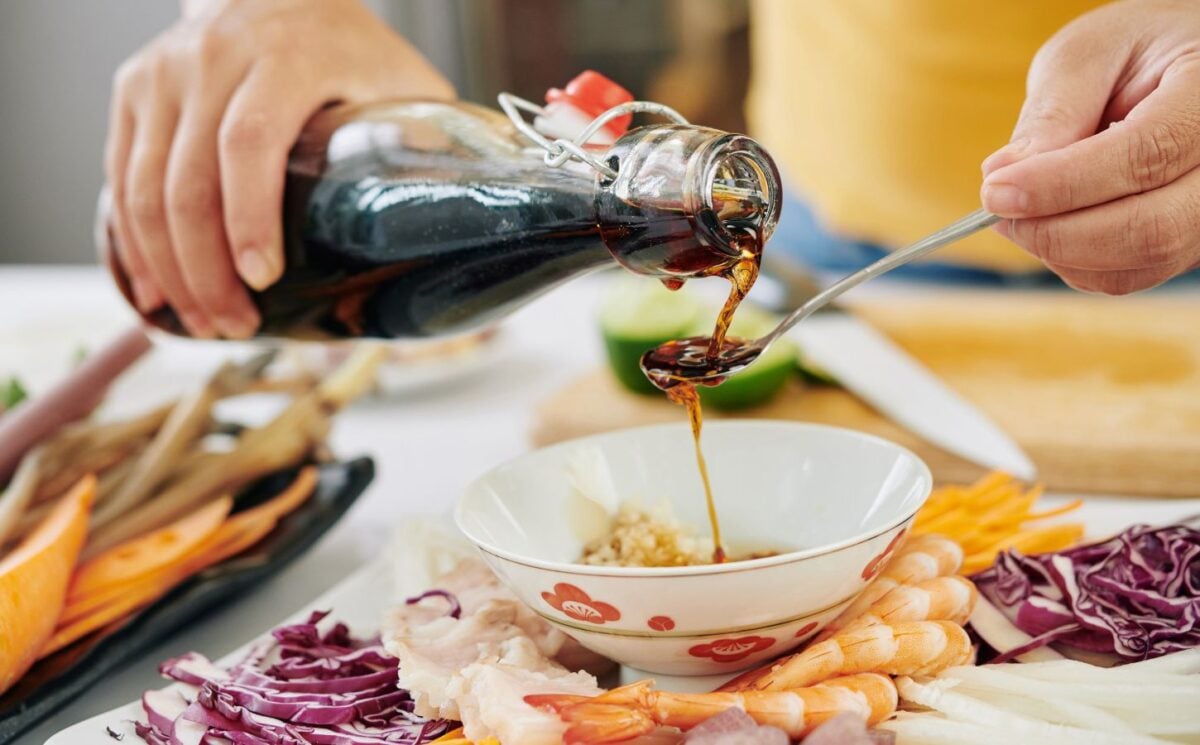 Photo shows someone pouring soy sauce from a glass bottle into a spoon