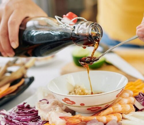 Photo shows someone pouring soy sauce from a glass bottle into a spoon
