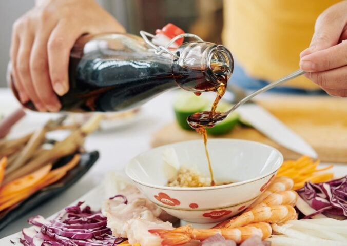 Photo shows someone pouring soy sauce from a glass bottle into a spoon