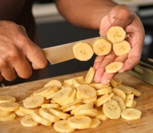Photo shows a young African man's hands as he chops plantain in the kitchen